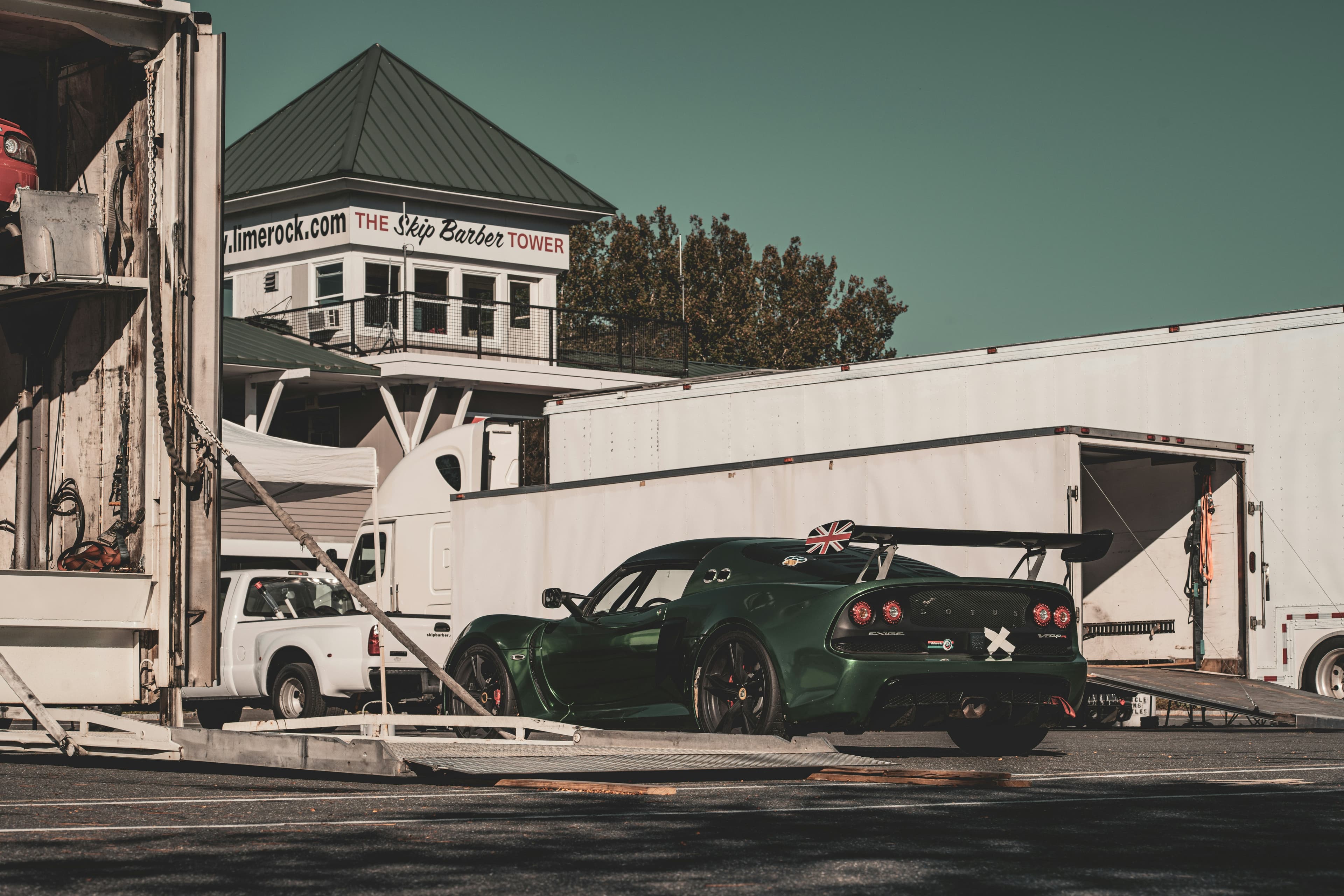 A green Lotus Exige race car parked near transport trailers at Lime Rock Park racetrack.